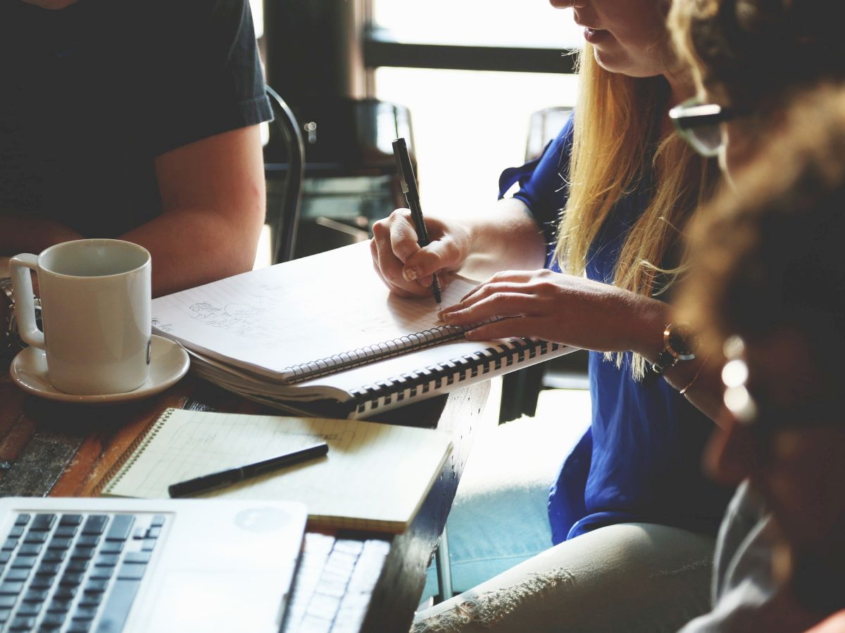 A group of people working together at a table with laptops, notebooks, and a cup, engaging in a collaborative discussion or meeting.