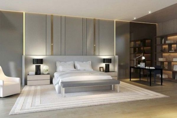 A modern bedroom features a bed with side tables, a chair, a desk with a lamp, and a bookshelf, showcasing neutral tones and sleek design.