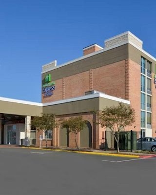 The image shows a hotel building with a covered entrance and a parking area.