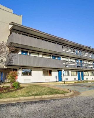 The image shows a three-story building with a Motel 6 logo, featuring outdoor corridors, accessible parking, and landscaped surroundings.