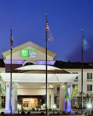 A hotel building at dusk with multi-story architecture, illuminated entrance, and three flagpoles in front.