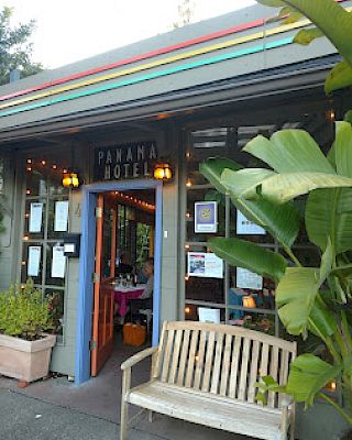 The image shows the entrance of the Panama Hotel with a bench and plants outside, featuring a colorful roof and various signs.