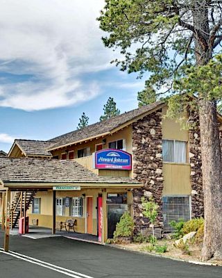 A two-story motel with a rustic facade surrounded by trees and a parking lot in front. The sign reads 