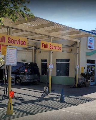 The image shows a full-service car wash with an awning and vehicles. A person is walking nearby with trees in the background.