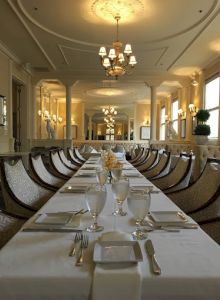 An elegant dining room with a long table set for a formal event, featuring chandeliers, large mirrors, and classic decor.